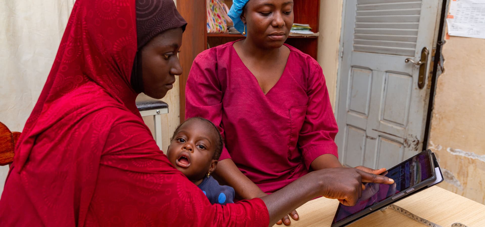 A patient with her child observes information shown by a midwife on a tablet.