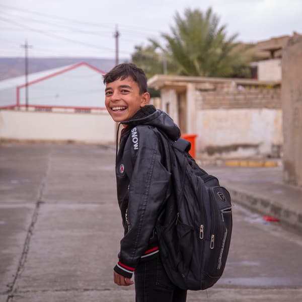 Young Zidan in the street, looks back over his shoulder and smiles at the camera.