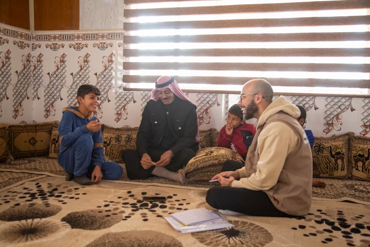 A Tdh staff member interviews a father and son. They are all seated on the floor.