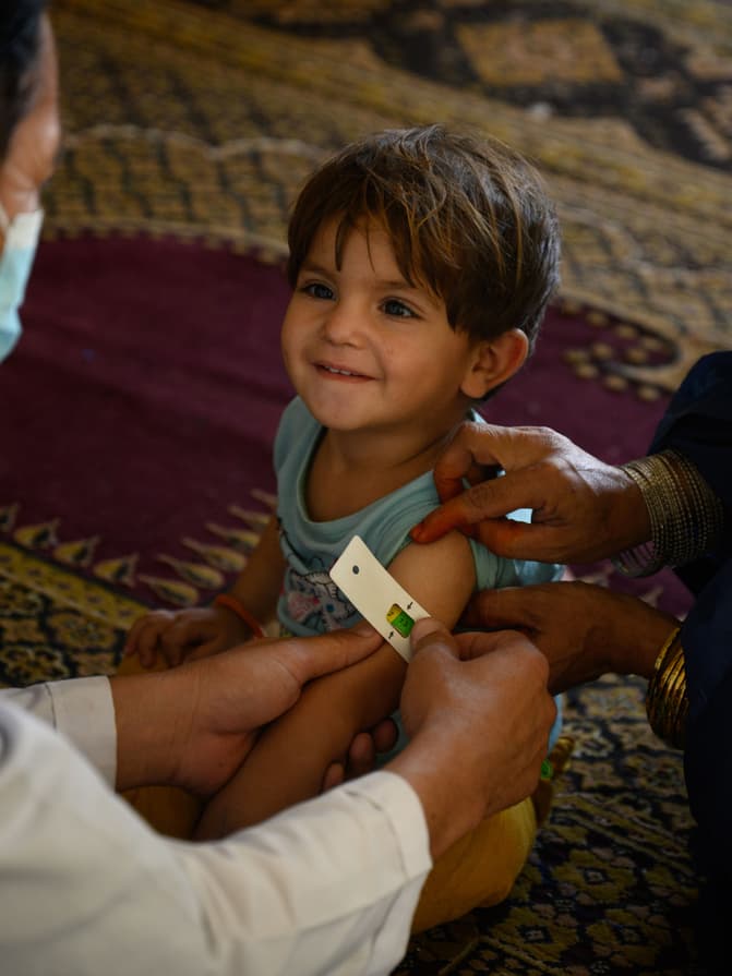 Un enfant souriant se fait mesurer le tour de bras.