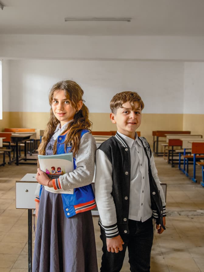 Une fille et un garçon debout devant une salle de classe vide.